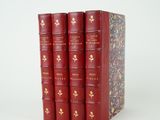 trois livres rouges ornés de lettres dorées, posés sur une surface blanche