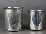 une paire de verres à shot en métal argenté posés sur une table avec un fond gris