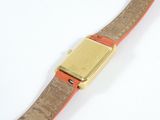 an image of a wrist watch with a gold plated case and orange leather band