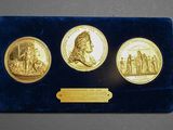 un gros plan sur trois pièces d'or posées sur une table, accompagnées d'une plaque