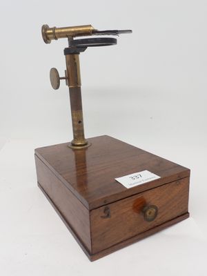 un microscope à l'ancienne posé sur une boîte en bois, sur fond blanc