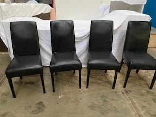 quatre fauteuils en cuir noir sont alignés contre un drap blanc