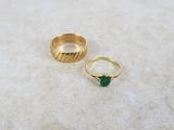 two gold rings with a green stone sitting on top of a white surface
