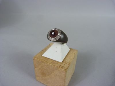 bague en argent massif sertie de grenatite et de diamants, posée sur un socle en bois