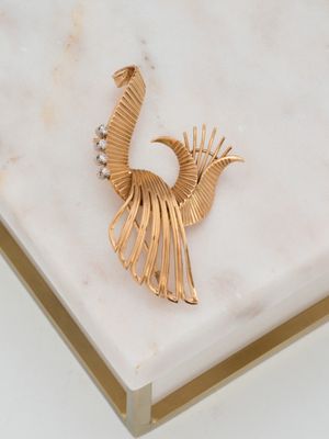 broche en forme de paon plaquée or posée sur un socle en marbre blanc