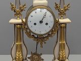 une horloge blanche et dorée posée sur un socle, elle-même posé sur une table