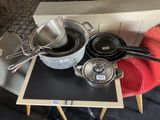 Plusieurs casseroles et poêles sont posées sur une table, accompagnées d'une étiquette de prix