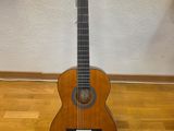 an acoustic guitar sits on a stand on a hard wood floor