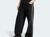 Un homme vêtu d'un pantalon noir et d'un t-shirt blanc se tient debout, les mains dans les poches.