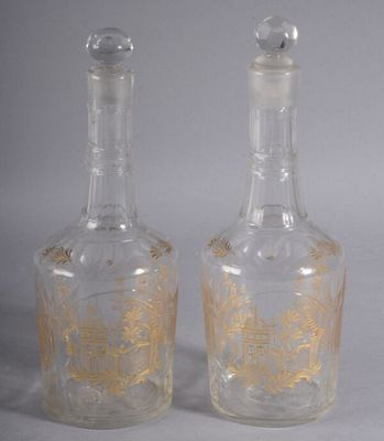 deux bouteilles en verre transparent ornées de motifs dorés, posées l'une à côté de l'autre