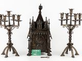 three metal candelabs with a clock on each of them