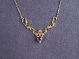 a close up of a gold necklace with a red stone