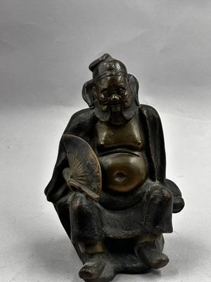 une statue représentant un homme assis sur une chaise, tenant un éventail