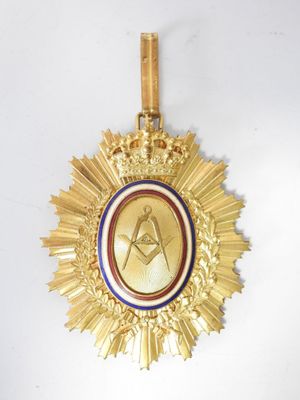 une médaille d'or ornée d'un symbole maçonnique, suspendue à un mur blanc