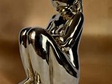 statue en argent représentant une femme assise à genoux sur un fond marron