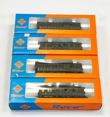 trois boîtes contenant des trains miniatures, posées sur une surface blanche