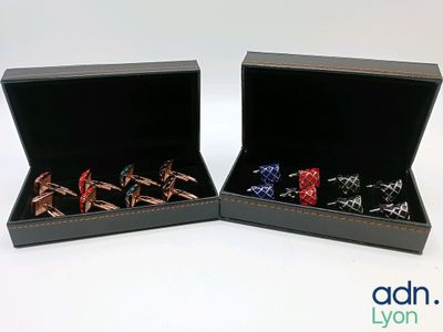 deux paires de bagues de manchette dans un coffret noir posé sur une surface blanche