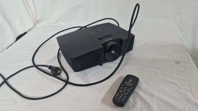 un projecteur noir posé sur un drap blanc, avec une télécommande