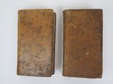 two old books are sitting side by side on a white surface