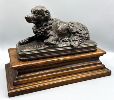 une statue en bronze représentant un chien couché sur un socle en bois