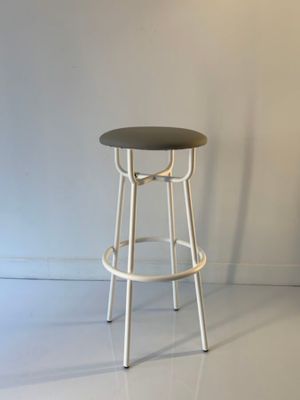 un tabouret noir posé sur un sol blanc, devant un mur blanc
