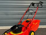 une tondeuse à gazon rouge aux roues jaunes garée devant un garage