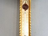 a gold clock hanging on the wall with a thermometer on it