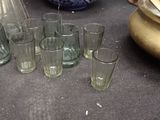 bottles and glasses on a table next to a pitcher and vase