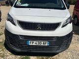 La petite camionnette blanche est garée sur la terre battue, près d'autres voitures.