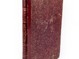 un vieux livre à la couverture rouge posé sur une surface blanche