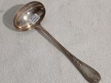 une cuillère plaquée argent posée sur une nappe blanche, sur laquelle est apposée une étiquette