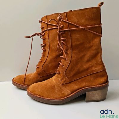 Bottes à lacets de couleur beige posées sur une surface blanche, avec un fond blanc
