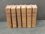 six old books are lined up on a black surface