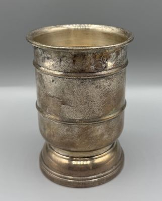 une coupe ancienne en métal argenté, posée sur un socle, sur une surface blanche