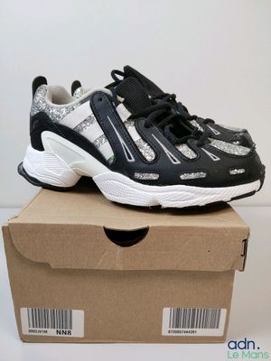 des baskets noires et blanches posées sur une boîte en carton, elle-même posée sur une surface blanche