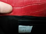 someone is holding a red leather purse with a label on it