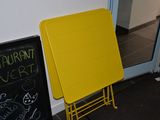 une table jaune posée à même le sol, à côté d'un tableau noir