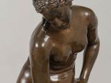 bronze statue of a woman sitting on a rock with her hands on her knees
