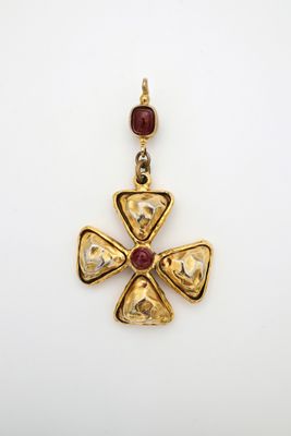 un gros plan d'un pendentif en forme de croix en or orné d'une pierre rouge