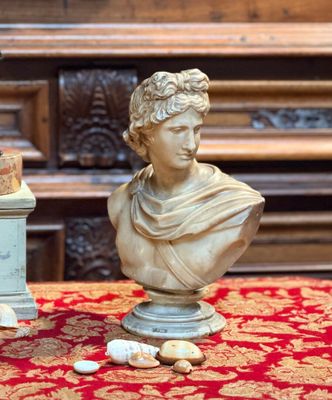 une statue représentant un homme assis sur une table, à côté d'un vase