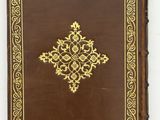 a brown book with gold trimming and a golden cross on it