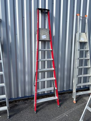 Plusieurs échelles sont alignées contre un mur métallique devant un immeuble.