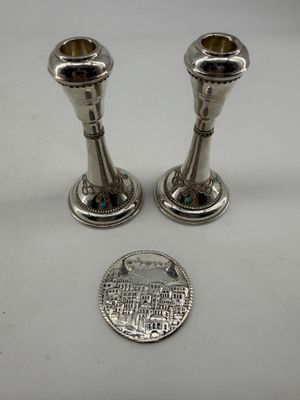 two silver candlesticks on a white surface next to a penny