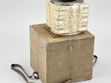 beige and black vase sitting on top of a box on a white surface