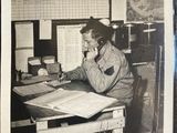 an old black and white photo of a man sitting at a desk with a phone to his ear