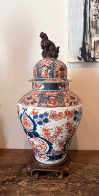 un grand vase posé sur une table en bois, avec un tableau accroché au mur derrière lui