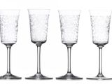 six empty wine glasses lined up in a row on a white surface
