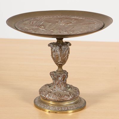 une image représentant une assiette en bronze posée sur une table en bois, sur laquelle se trouve un oiseau