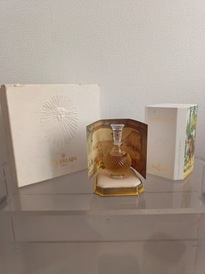 une étagère en verre sur laquelle sont posés un flacon de parfum et une boîte