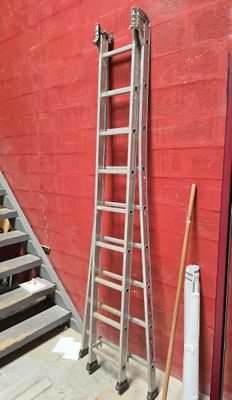 une échelle appuyée contre un mur rouge, à côté d'un escalier